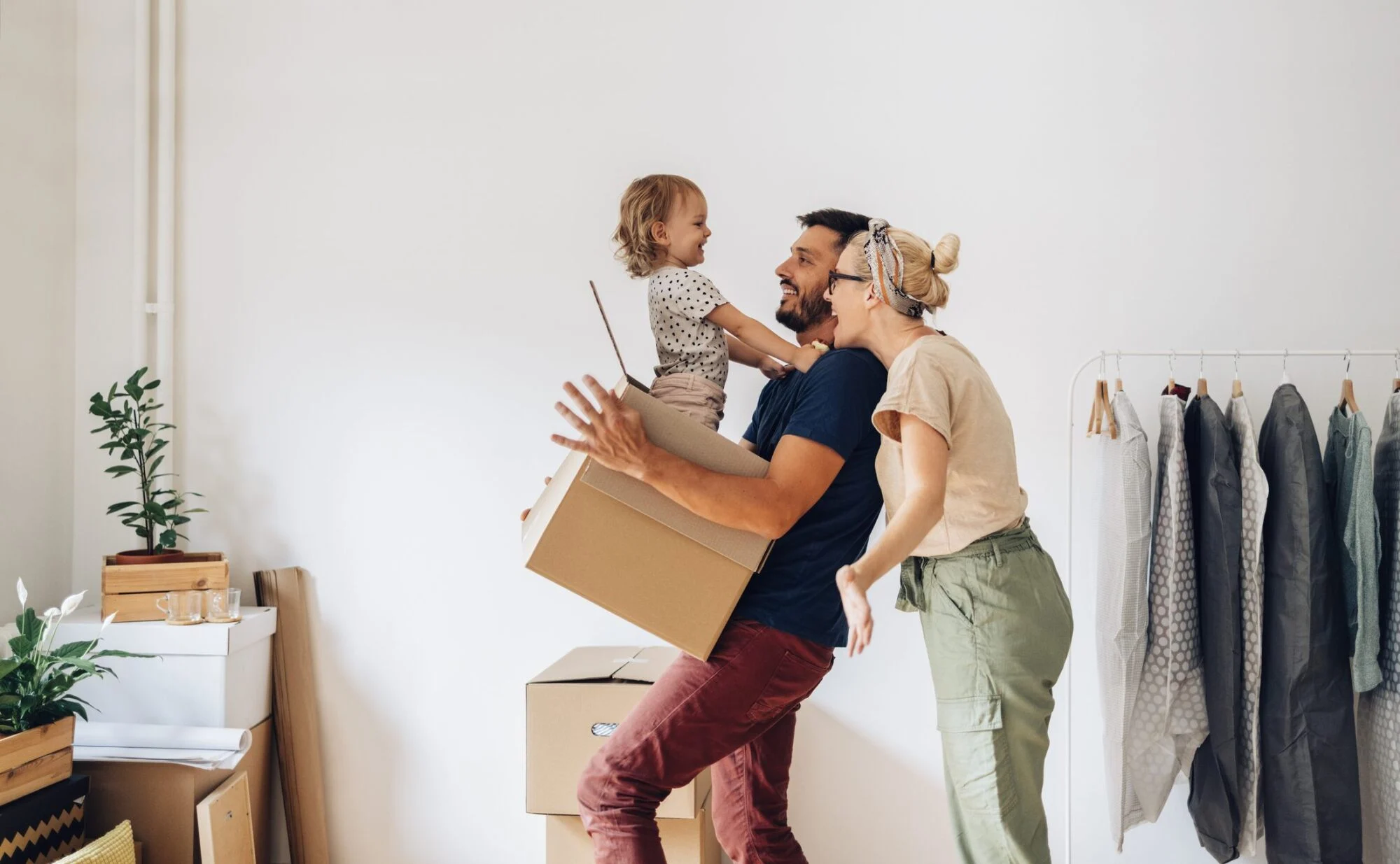 A smiling family carries moving boxes in a new home, with a child laughing in a parent's arms.
